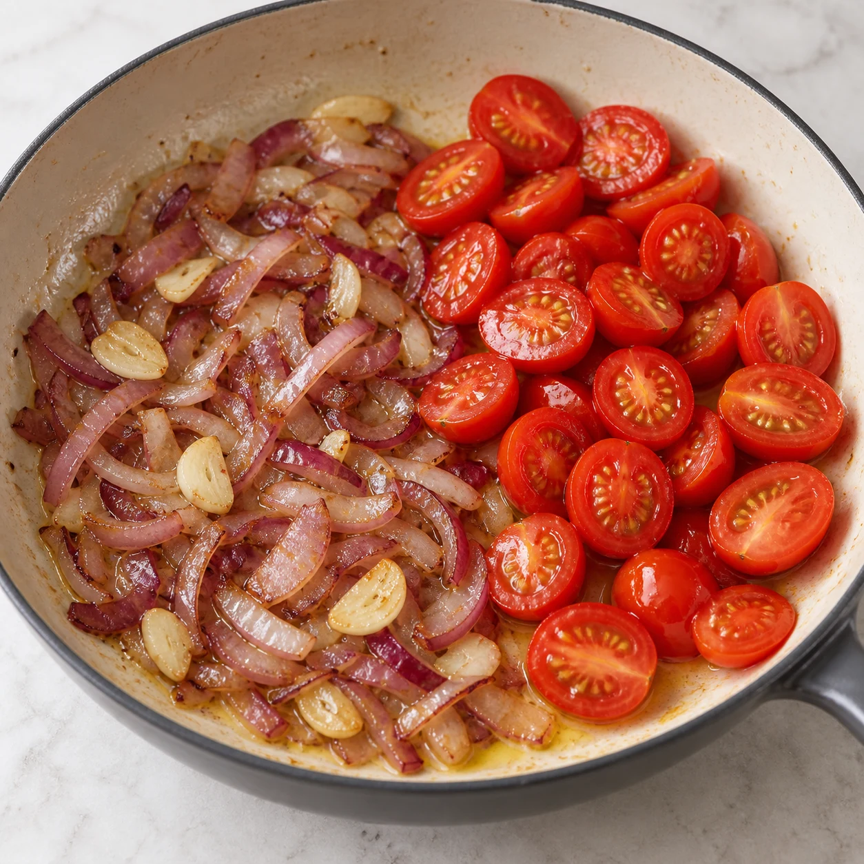 Photo culinaire carrée en lumière naturelle : oignon rouge et ail émincés légèrement colorés dans l’huile d’olive, demi-tomates cerise préparées à côté dans la poêle, aucun autre ingrédient visible, aucun texte, aucune marque.