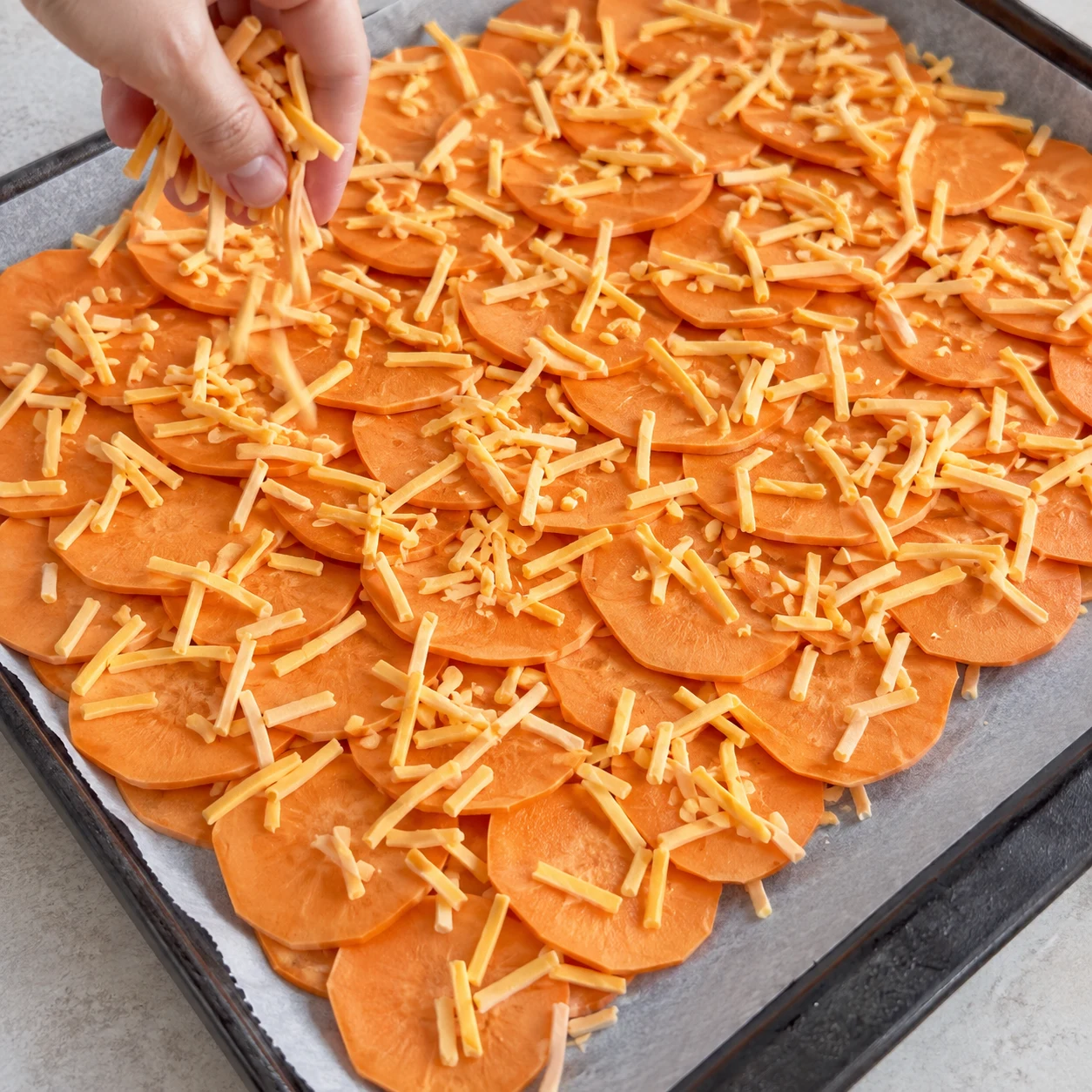 Une main anonyme répartit des fines lanières végétales jaune-orange sur les rondelles de patate douce crues.