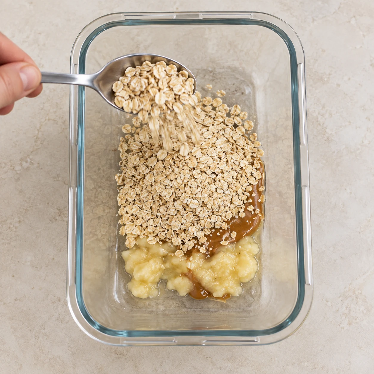 Une cuillère ajoute les flocons secs au récipient contenant banane et purée de cacahuète.