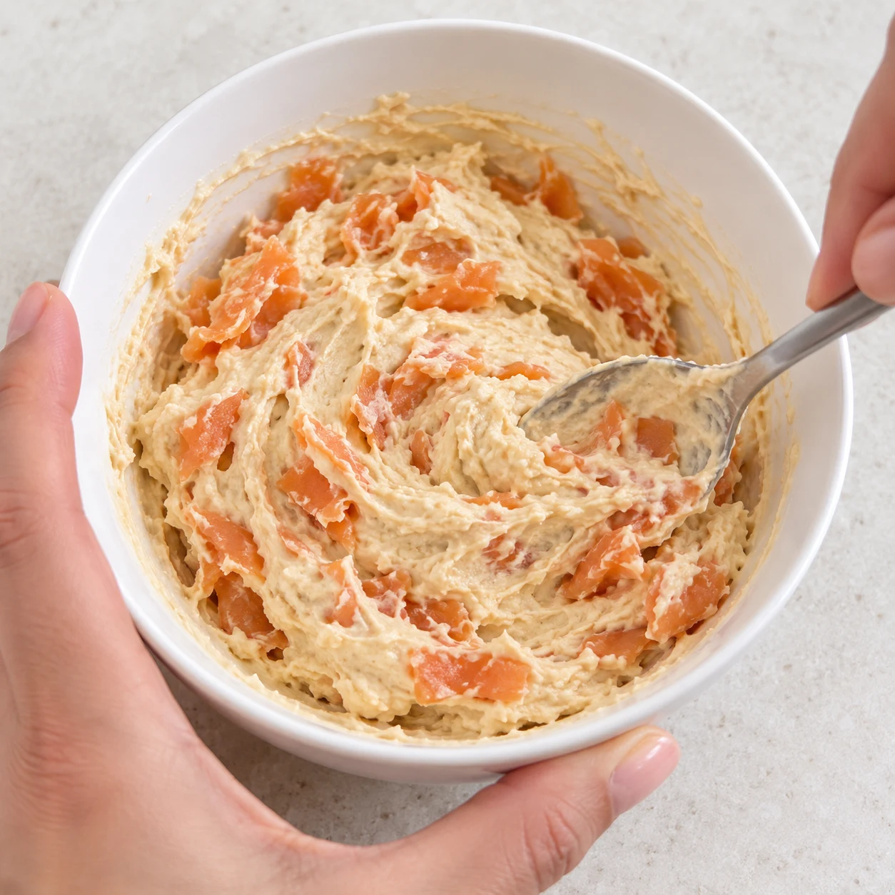 Cuillère mélangeant une crème de houmous beige avec des petits morceaux de saumon végétal orange.