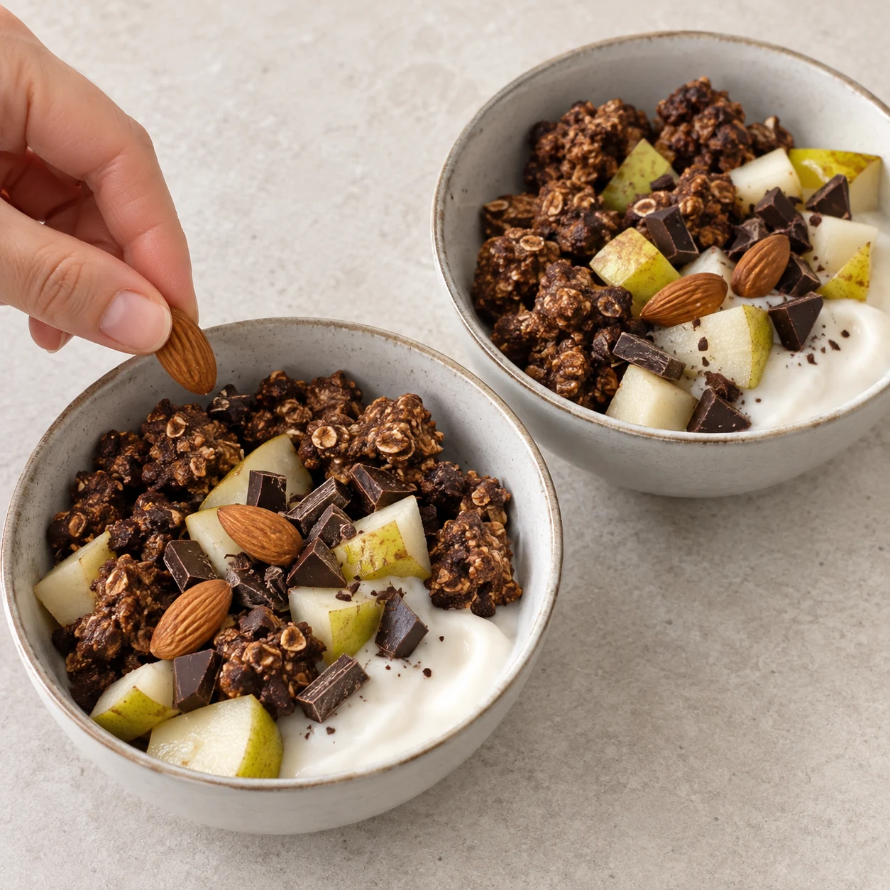 Deux bols de muesli en morceaux bruns, yaourt soja blanc, poire avec peau, quelques amandes seulement et éclats de chocolat noir ; aucune autre noix.