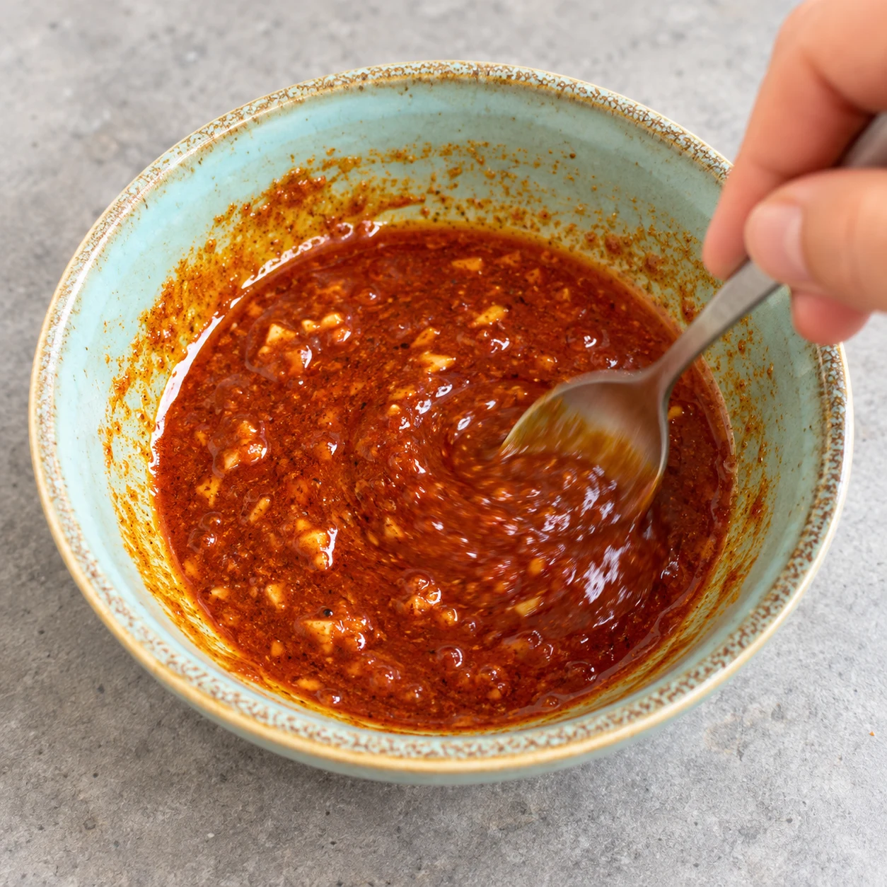 Mélanger la marinade : La marinade est homogène et rouge orangé, avec l’ail réparti dans l’huile.