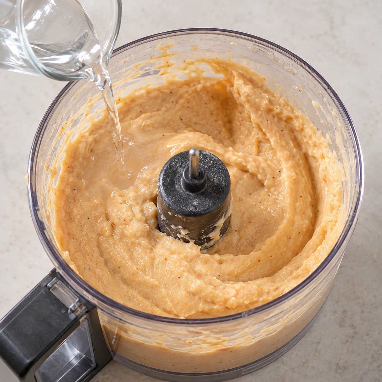Petit filet d’eau ajouté à une crème de haricots beige orangée dans un bol de robot débranché.