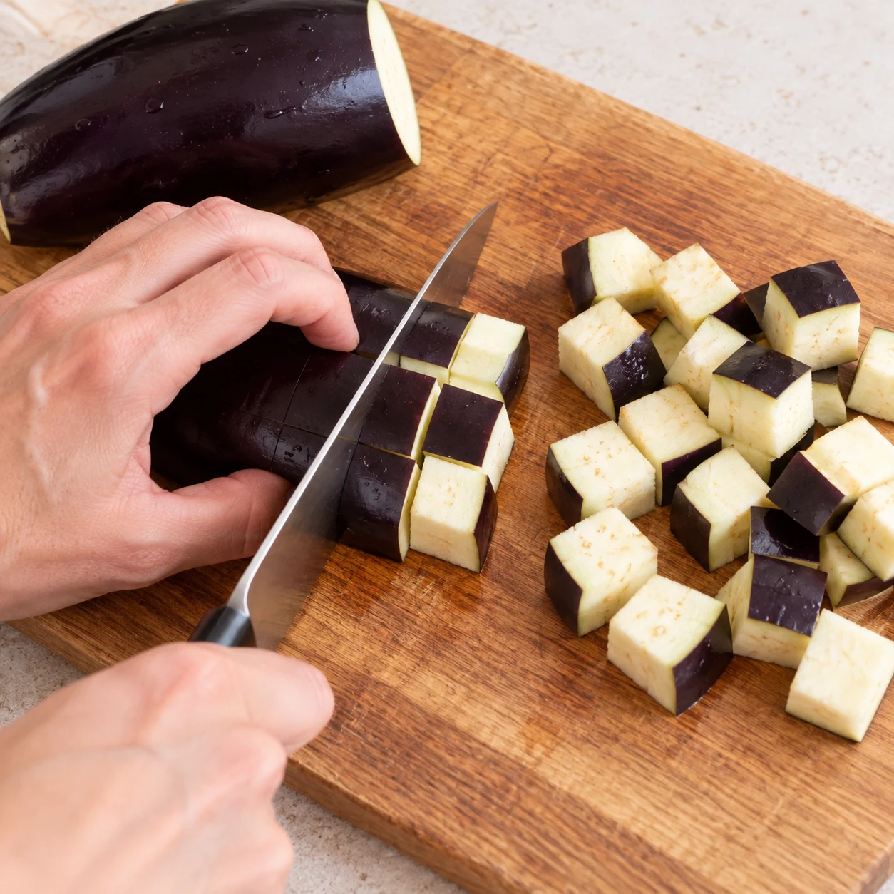 Main anonyme en griffe ; couteau coupant l’aubergine en cubes ; peau violette.