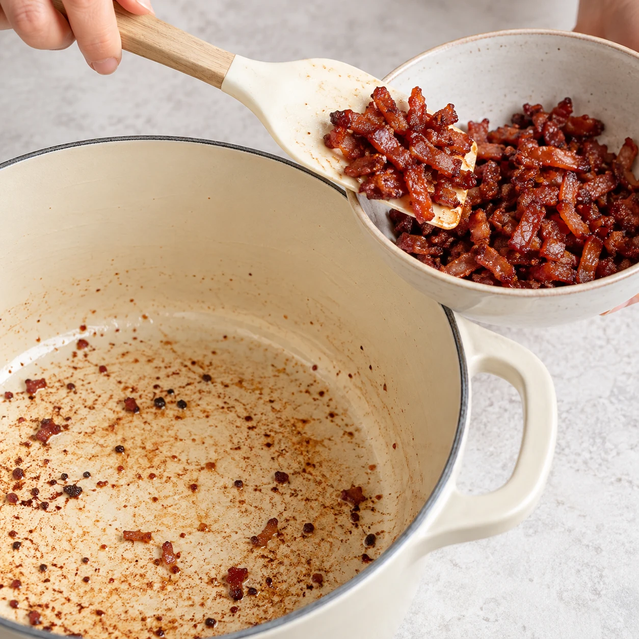 Photographie carrée de livre de recettes, une seule action : Réserver les lardons grillés. Retirez les lardons grillés de la cocotte avec une spatule et gardez-les dans un bol jusqu’à la fin de la cuisson. État attendu : Les lardons sont dans un bol et la cocotte est libre pour les poireaux. Montrer exclusivement Lardons végétaux fumés. Cocotte émaillée crème et plan de travail pierre pâle, lumière naturelle. Le bacon, le cheddar et les laitages de la capture source sont remplacés par les ingrédients végétaux documentés. Aucun texte, marque, bijoux, visage, corps ou identité de la personne.