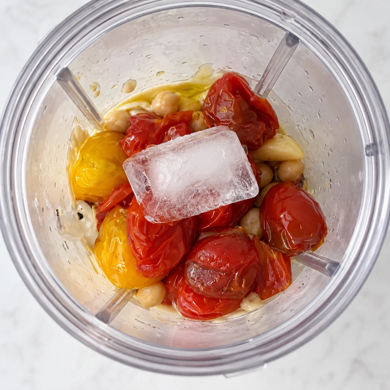 Glaçon translucide déposé sur les tomates rôties dans le bol du mixeur.