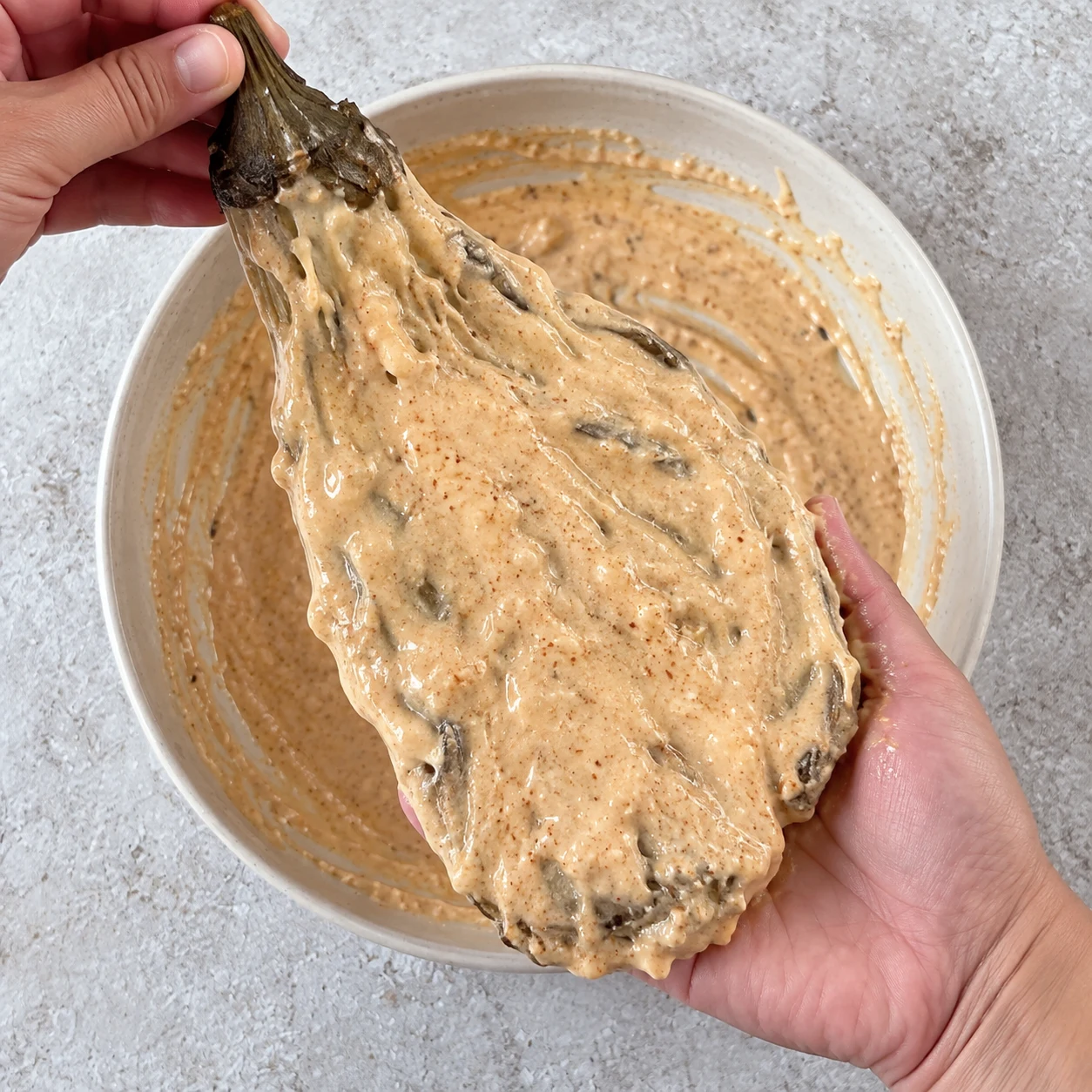 Enduisez les deux faces de l’aubergine aplatie de pâte assaisonnée, en la soutenant pour ne pas la déchirer. Montrer une seule phase de préparation, sans texte et sans personne identifiable.