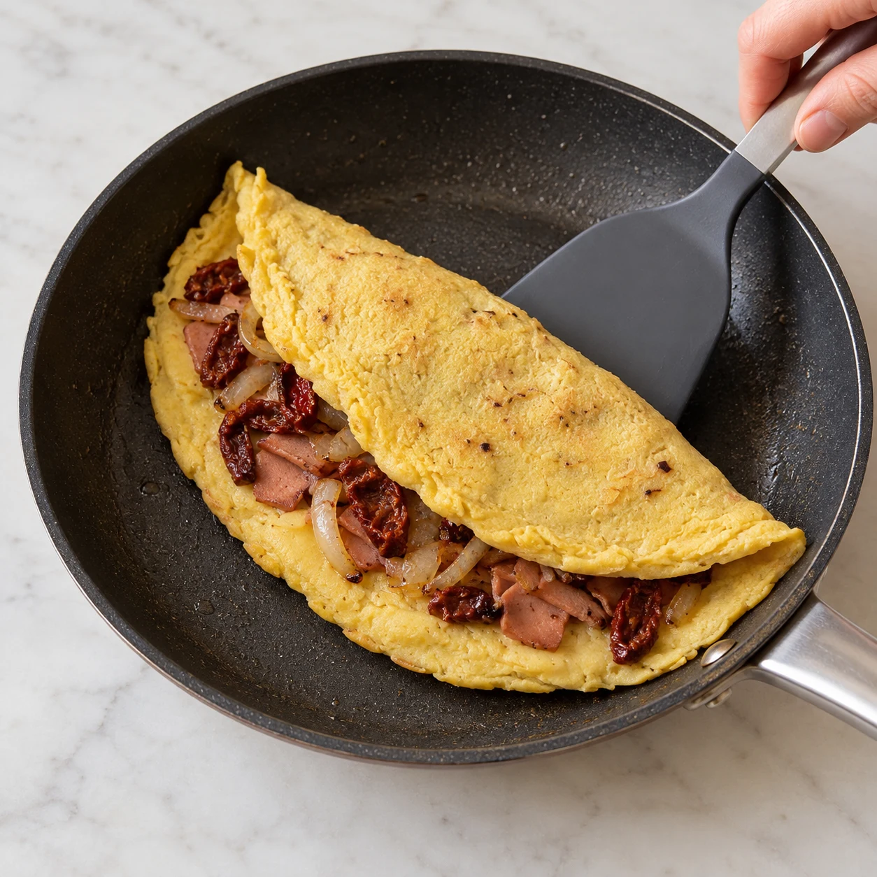 Omelette jaune pâle cuite repliée à la spatule dans une poêle, garniture visible à l’ouverture.