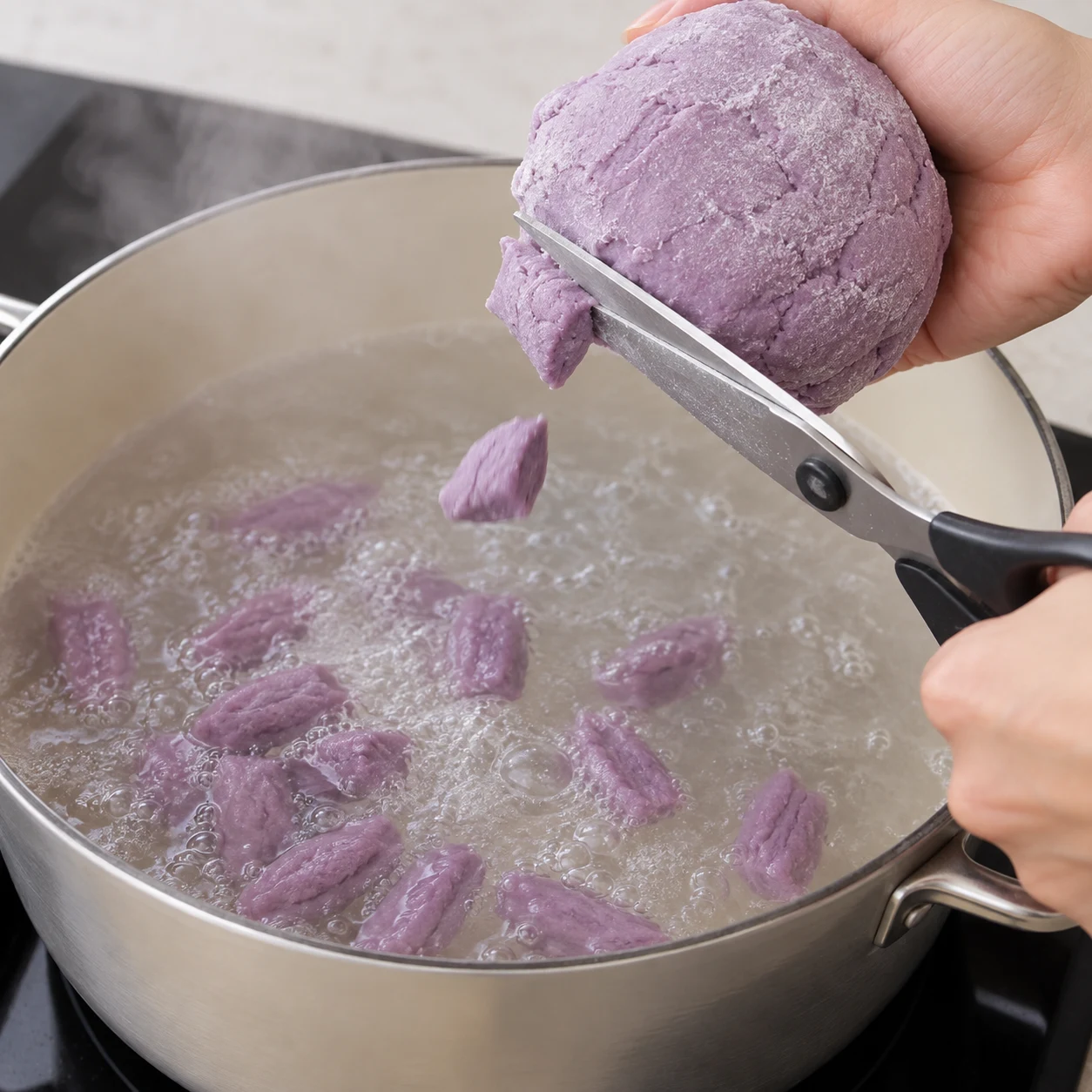 Ciseaux coupant une boule de pâte mauve en morceaux courts au-dessus d’une casserole.
