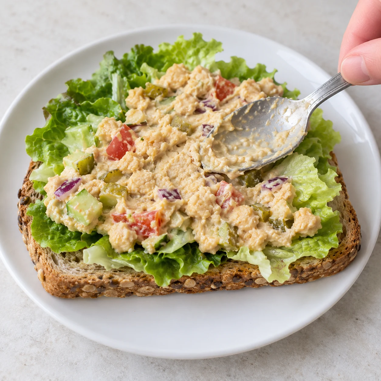 Étalez la moitié de la garniture crémeuse sur les feuilles de salade. Montrer uniquement les ingrédients de cette phase sur pierre pâle, vaisselle blanche neutre.