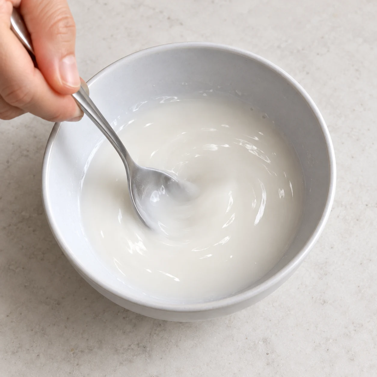 Mélange la cuillère à soupe bombée de fécule avec les 100 ml d’eau dans un petit bol. Une seule phase, sans texte ni personne identifiable. Pour la variante, montrer du tofu émietté et jamais des granulés secs, du doubanjiang ou des baies de Sichuan.