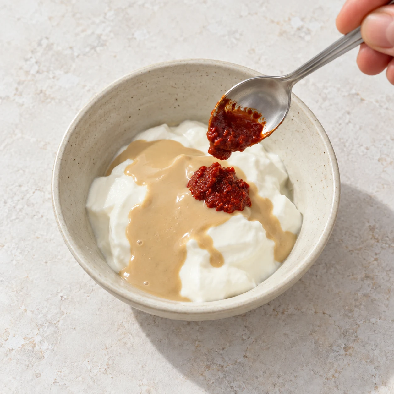 Petite touche de harissa rouge dans le bol de yaourt et tahini ; illustration de son ajout décrite dans la recette d’origine, le geste n’étant pas visible dans la capture.