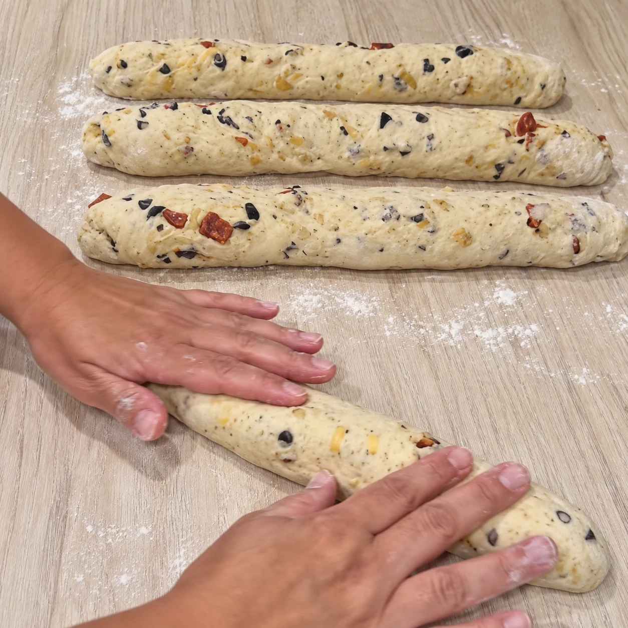 Allonger les baguettes. Quatre baguettes allongées, d’épaisseur régulière, sont formées. Respecter la capture source ; chorizo et cheddar uniquement végétaux, aucune autre garniture.
