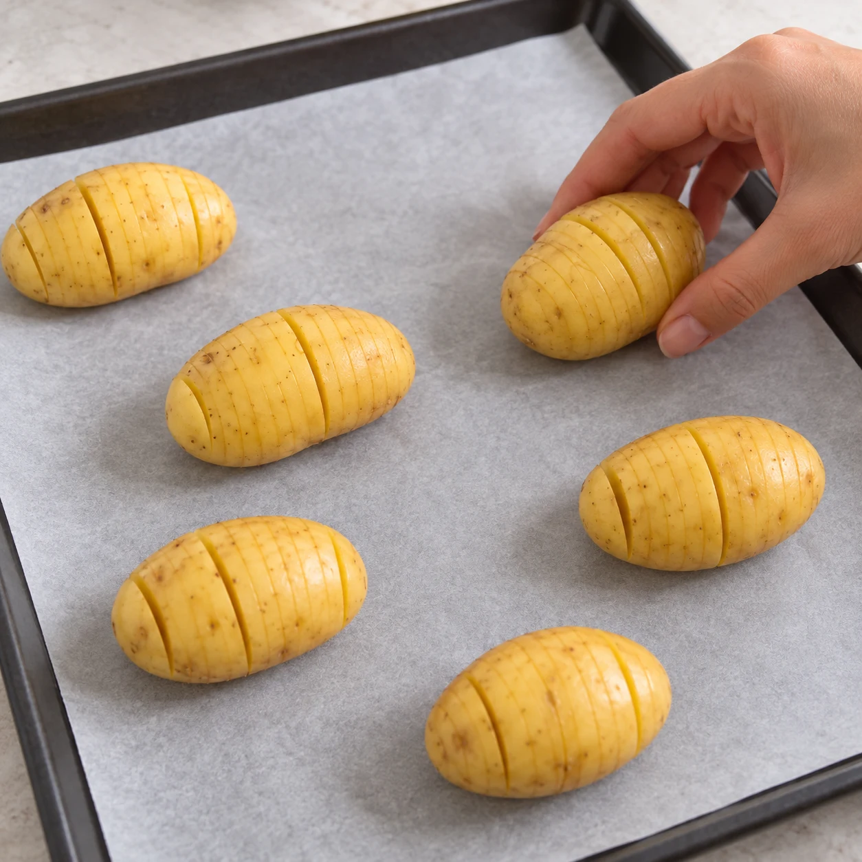 Main anonyme déposant une pomme de terre entaillée sur papier cuisson.