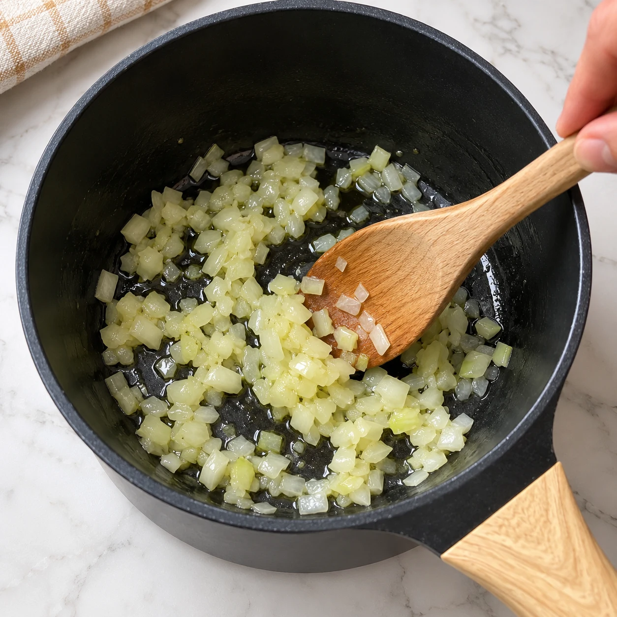 Casserole noire avec oignons hachés dans un film d’huile, spatule en bois.