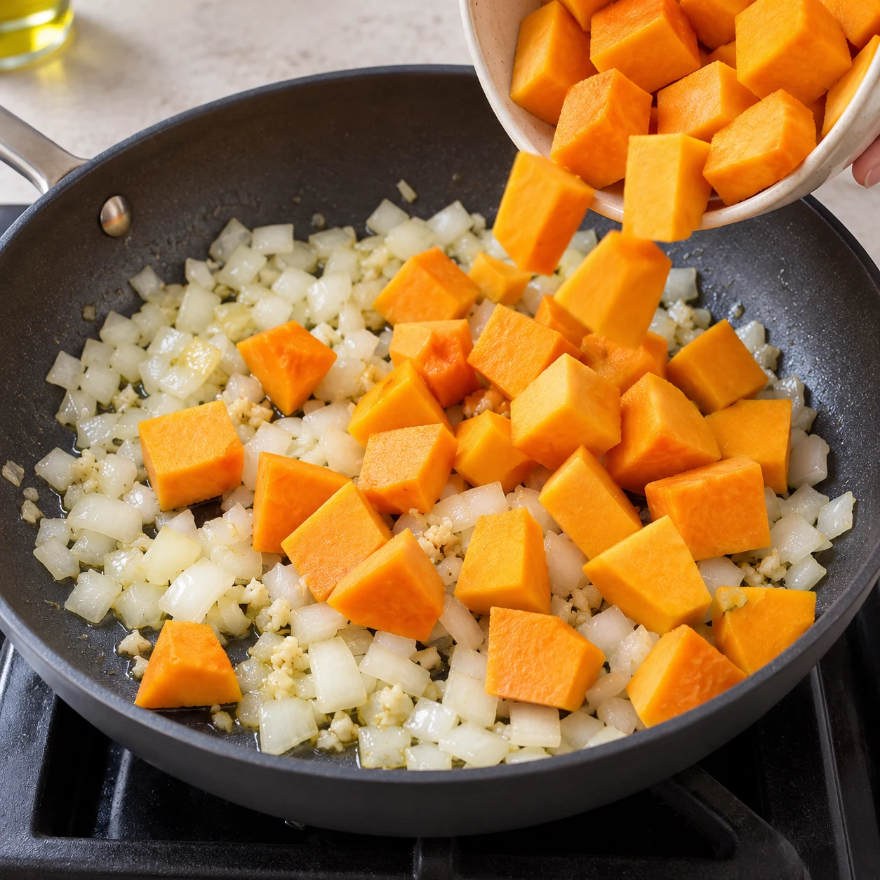 Cubes de courge crus versés dans la poêle contenant oignon et ail, pas de sauce.