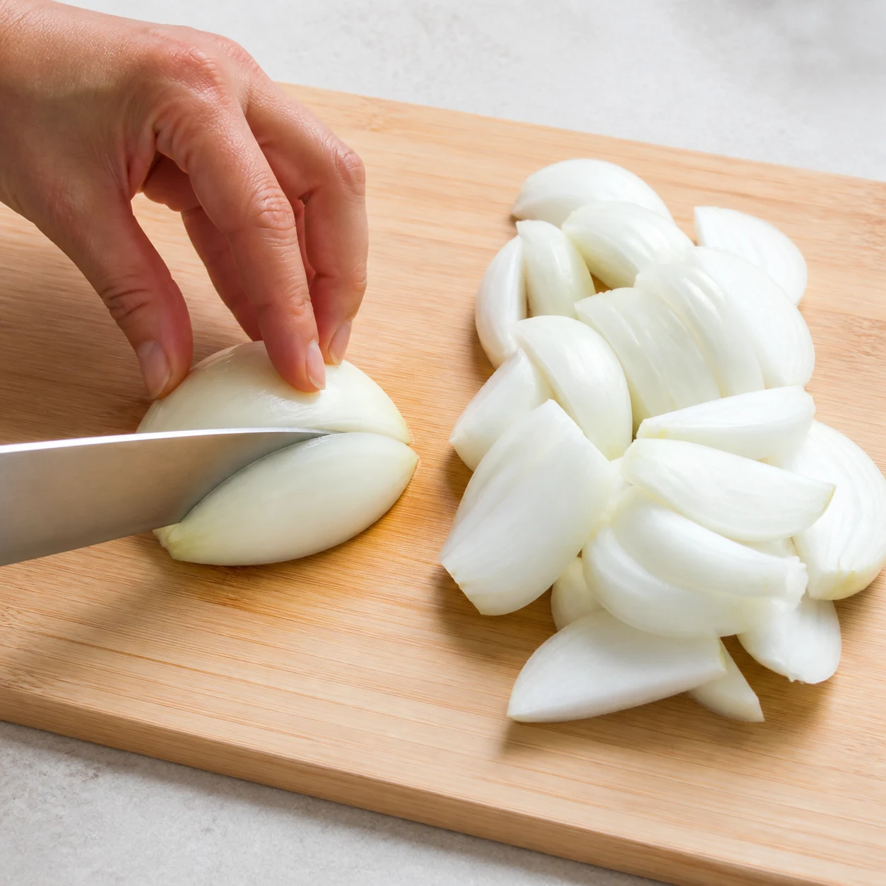 Oignons épluchés et coupés en morceaux réguliers sur une planche claire, sans autre légume.