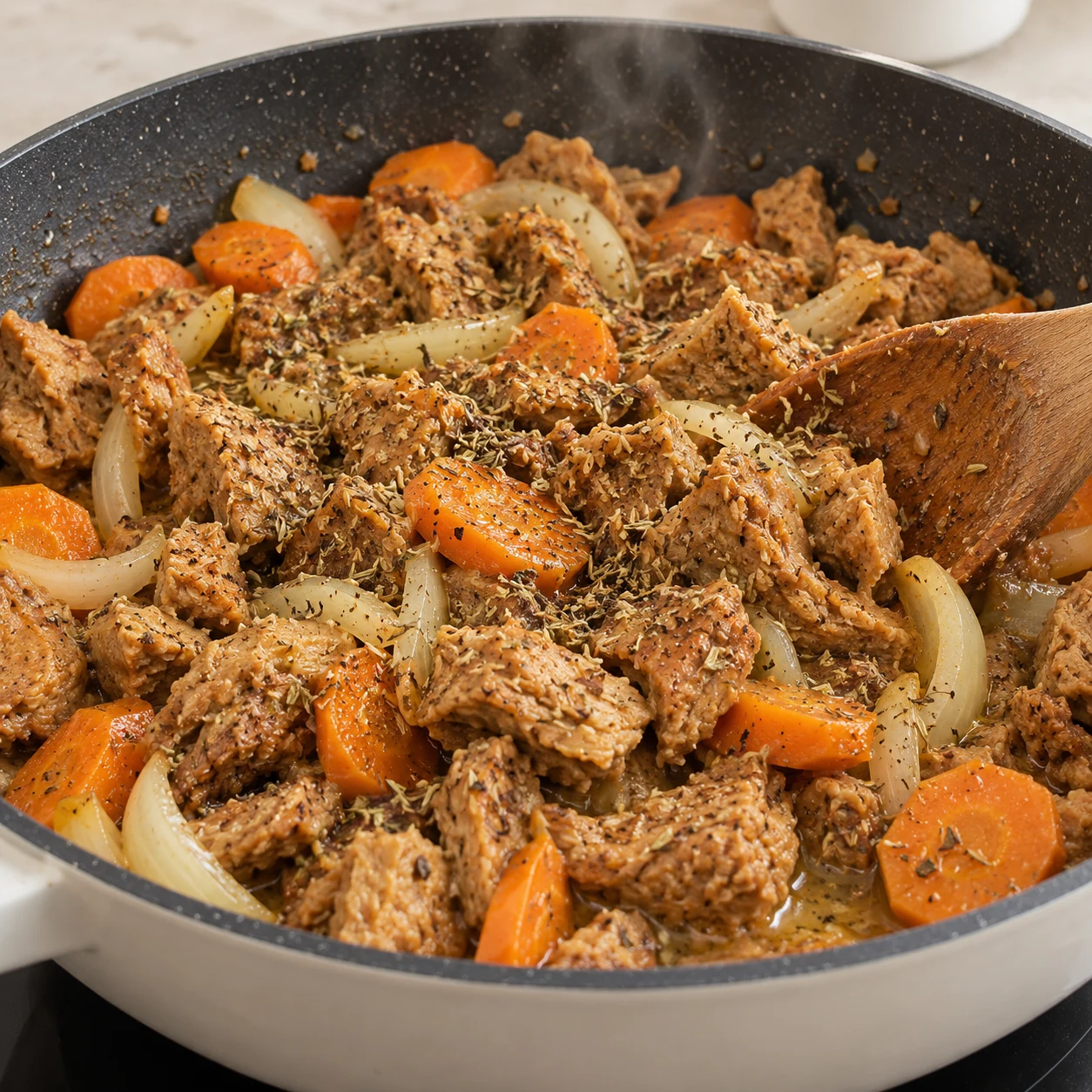 Morceaux de steak végétal ajoutés sur les carottes et oignons dans la sauteuse, saupoudrés d’herbes de Provence et de poivre, noix de beurre végétal qui fond.