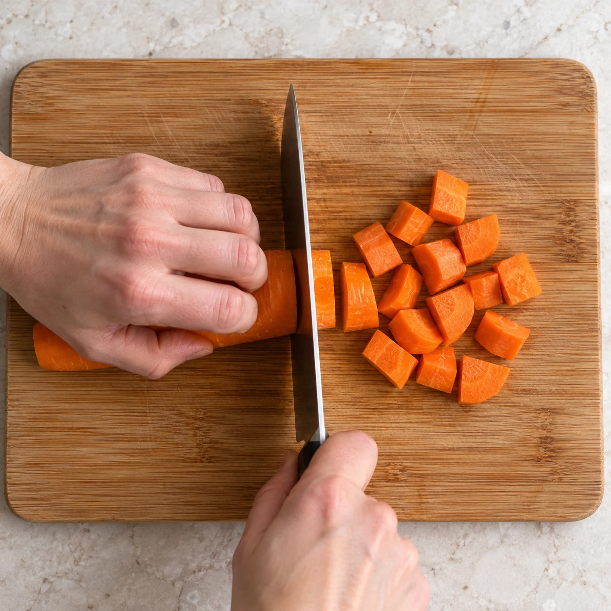 Une photographie carrée : Coupe la carotte en petits morceaux, comme dans la recette d’origine, sur une planche stable. Replie les doigts de la main qui la maintient. Résultat : Les morceaux de carotte ont une taille régulière.. Aucun ingrédient futur. Le Cayenne remplace le piment fumé original ; pas de piment fumé ajouté.