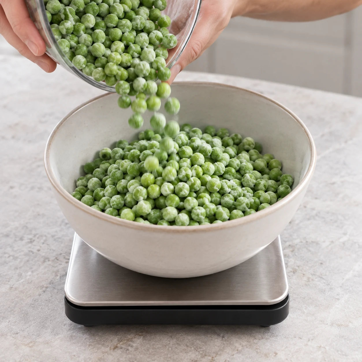 400 g de petits pois surgelés verts dans un bol posé sur une balance sans affichage lisible. Mains adultes anonymes versant les pois, cadrage carré. Aucun pois chiche, aucune gousse, aucun autre ingrédient.