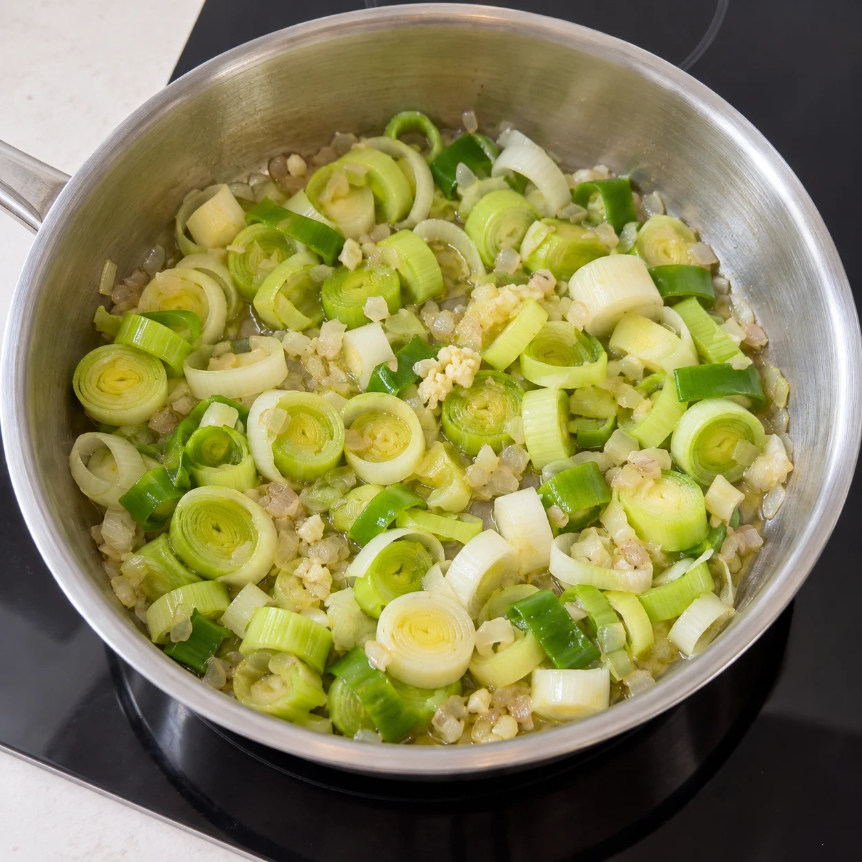 Versez les rondelles de poireaux rincées dans la casserole avec les aromates. Montrer seulement cet état, sans personne identifiable, visage, texte, logo ni ingrédient futur.