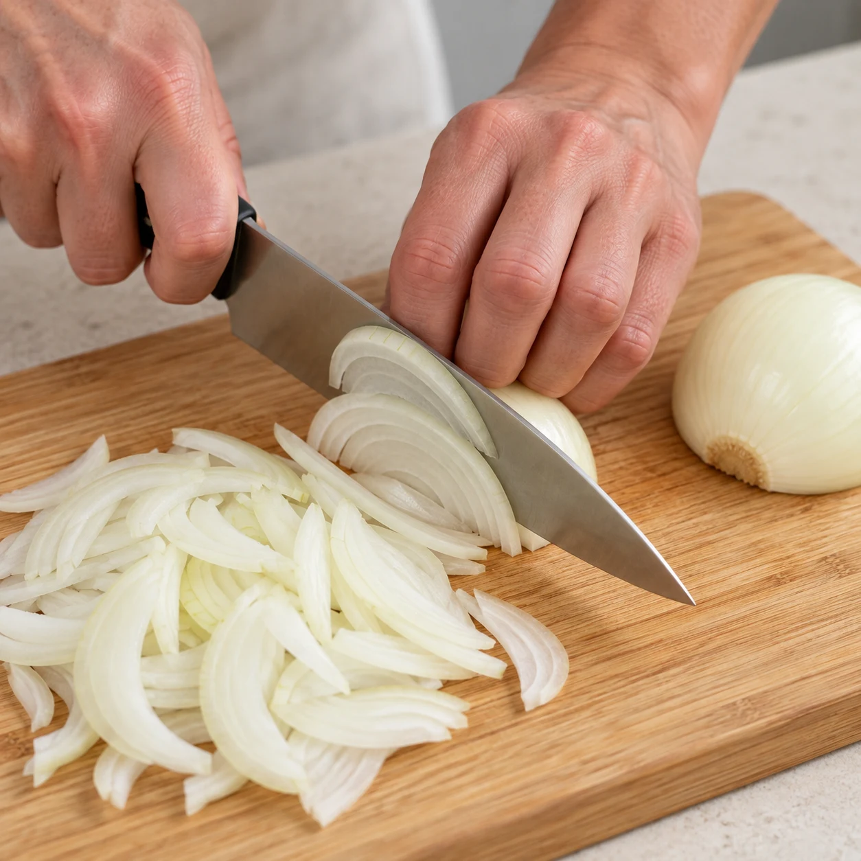 Pendant la cuisson, émince les deux oignons épluchés sur une planche stable, en gardant les doigts repliés loin du fil du couteau. Résultat attendu : Les deux oignons sont découpés en fines lamelles.
