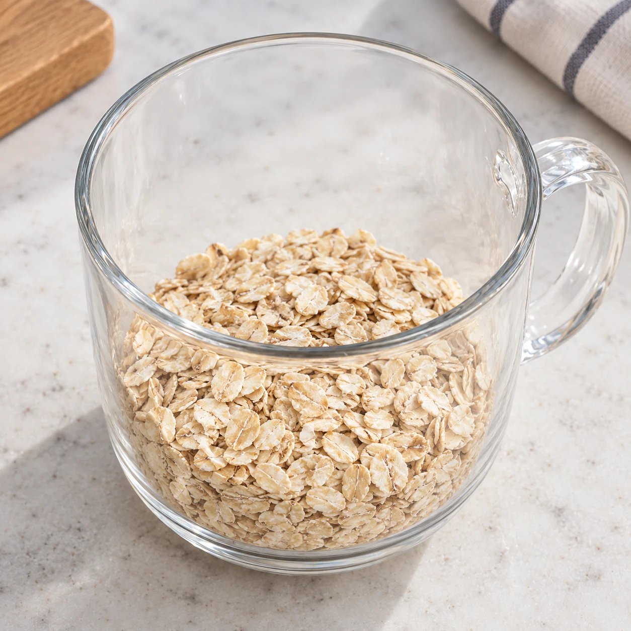 Dans un récipient, réunissez les 80 g de flocons d’avoine de base et les 20 g de flocons supplémentaires de cette recette bis. Montrer seulement cette phase de la variante à l’avoine, sans graines ni poudre, un récipient transparent à poignée sur pierre pâle, sans texte ni personne identifiable.