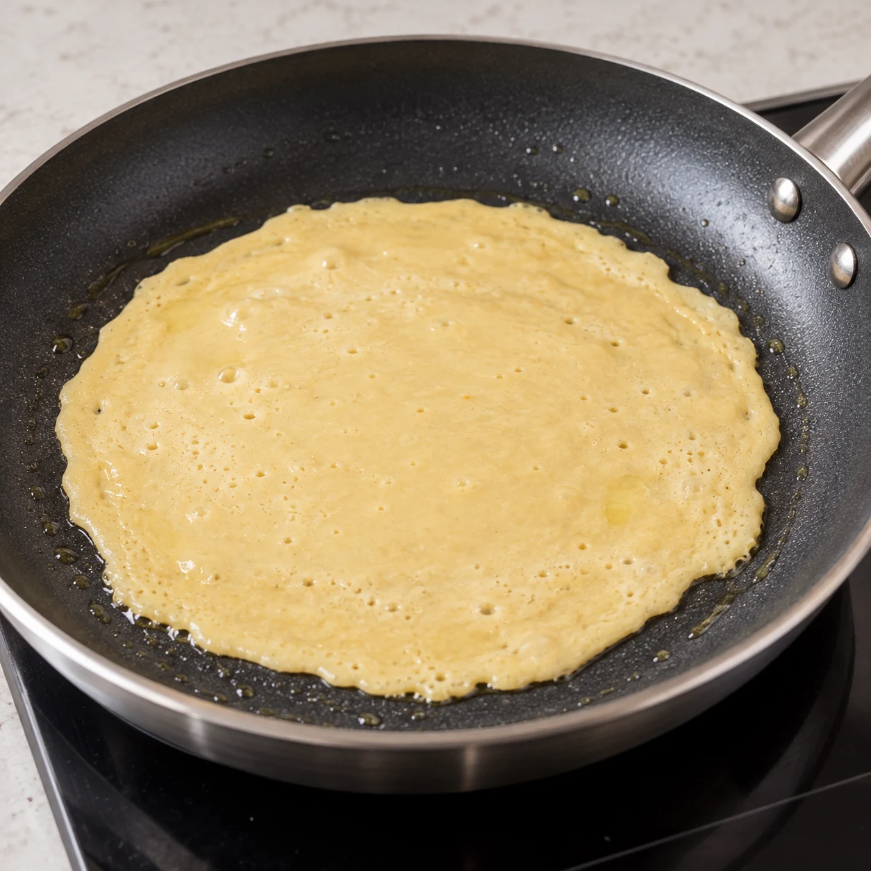 Fine galette beige de pois chiche en train de prendre dans une poêle antiadhésive.