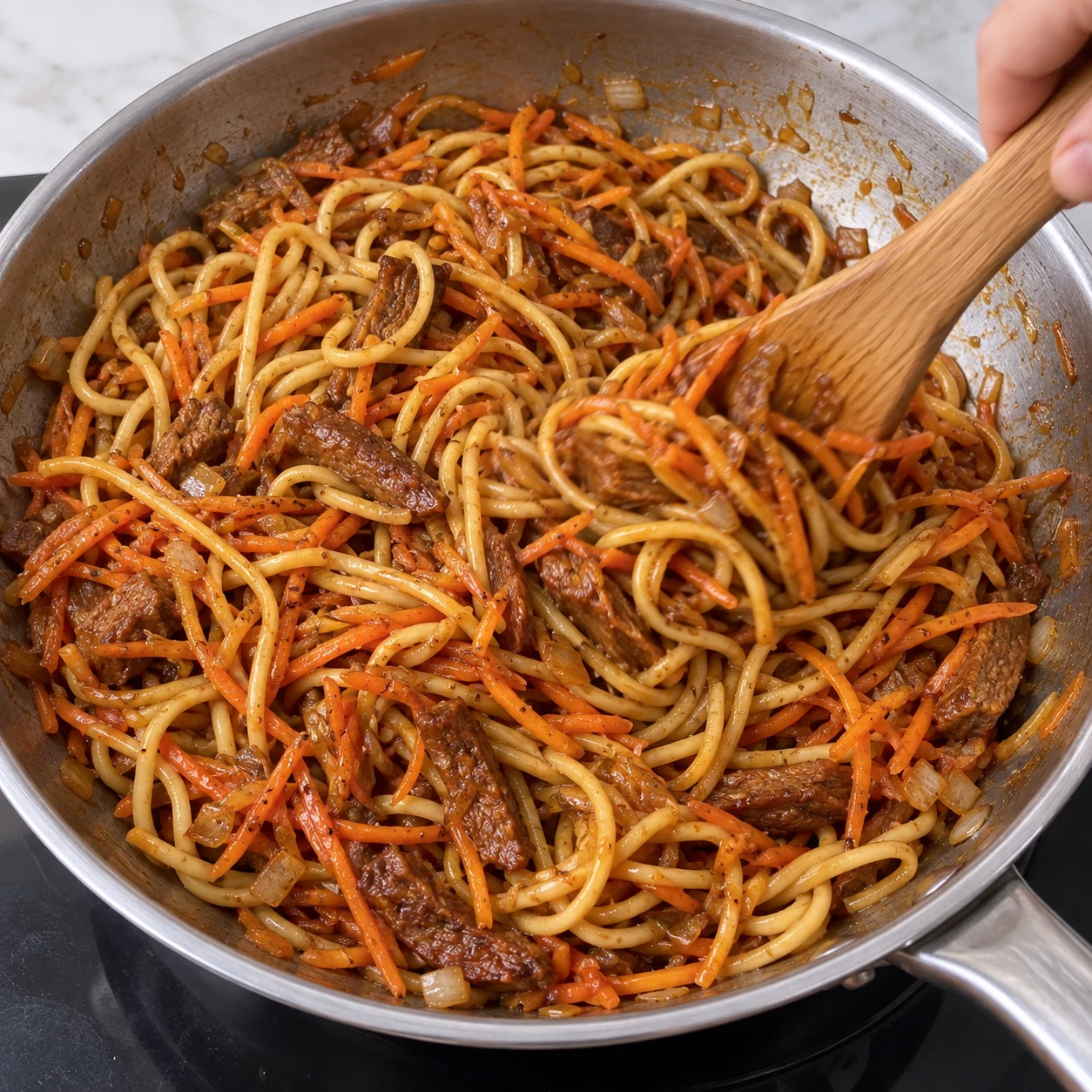 Main anonyme mélangeant des carottes râpées aux nouilles en sauce et aux lamelles végétales dans la poêle, sans ciboulette.