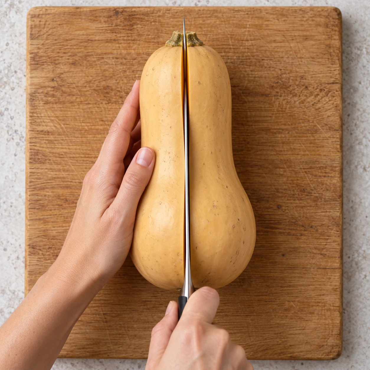 Coupe longitudinale active d’une courge butternut sur une planche stable, deux mains adultes anonymes; aucune farce.