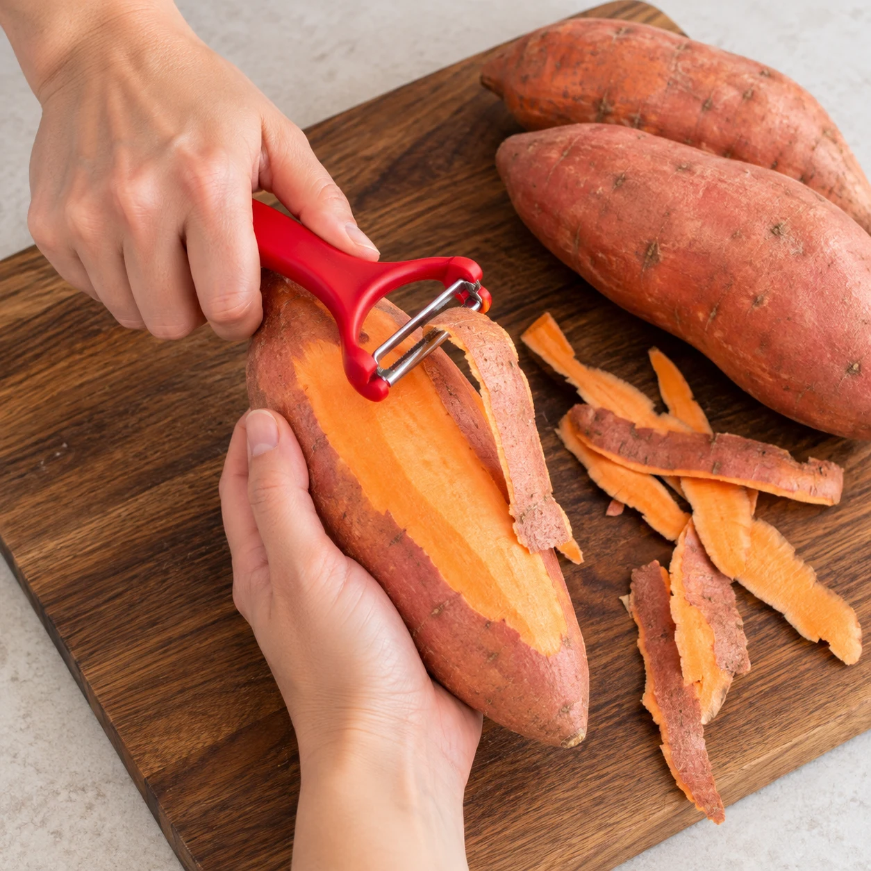 Économe retirant une bande de peau de patate douce, mains anonymes, planche stable.