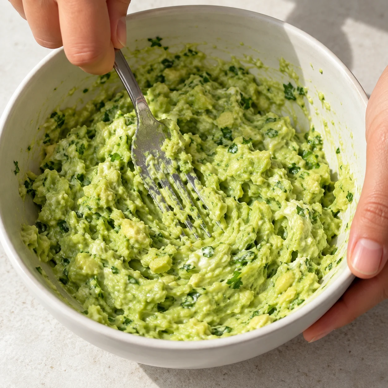 Cuillère écrasant une crème d’avocat vert clair avec yaourt et herbes hachées, sans tofu nature ni tortillas.