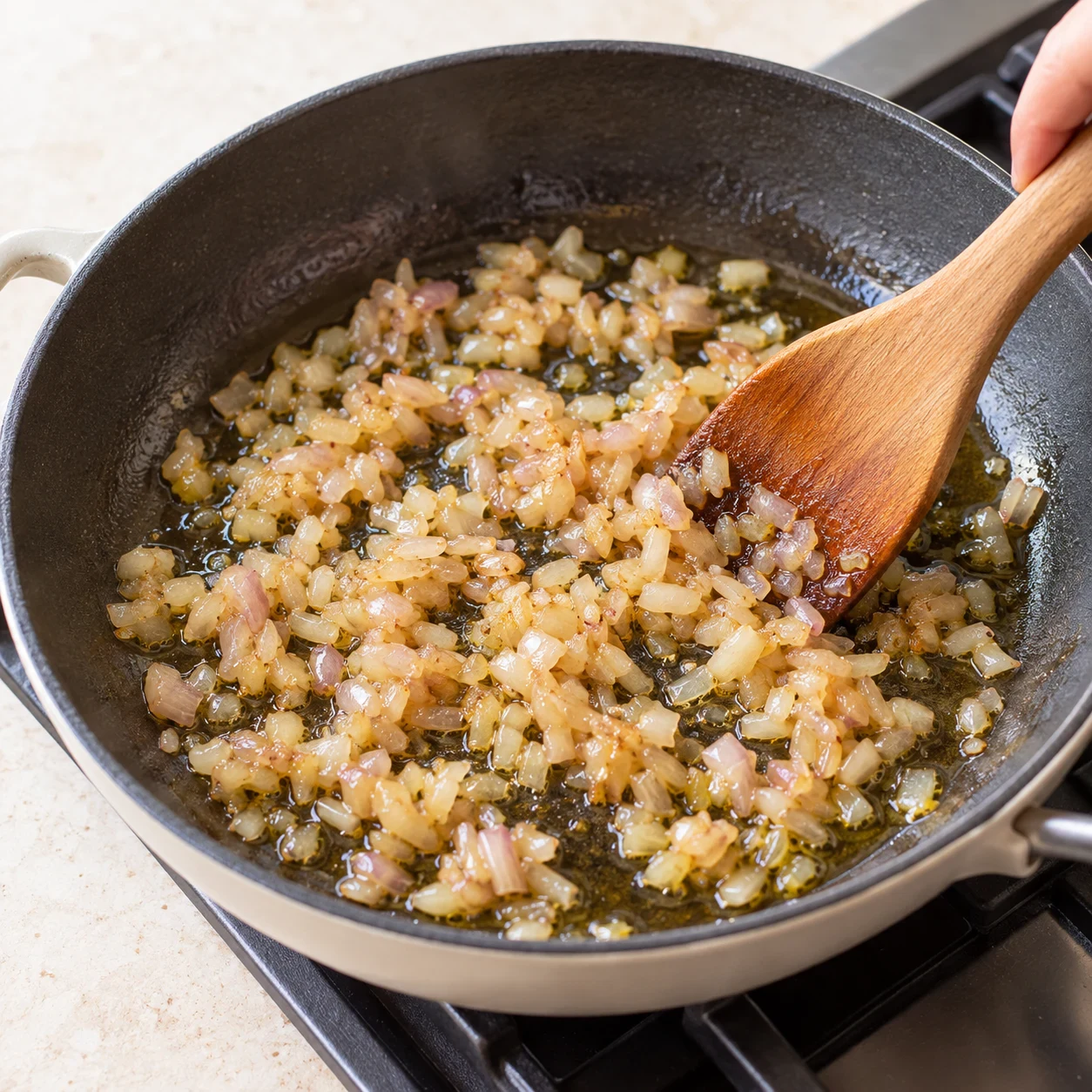 Photo culinaire carrée en lumière naturelle : échalote finement ciselée, souple et légèrement dorée dans une poêle avec l’huile d’olive, aucun autre ingrédient visible, aucun texte, aucune marque.