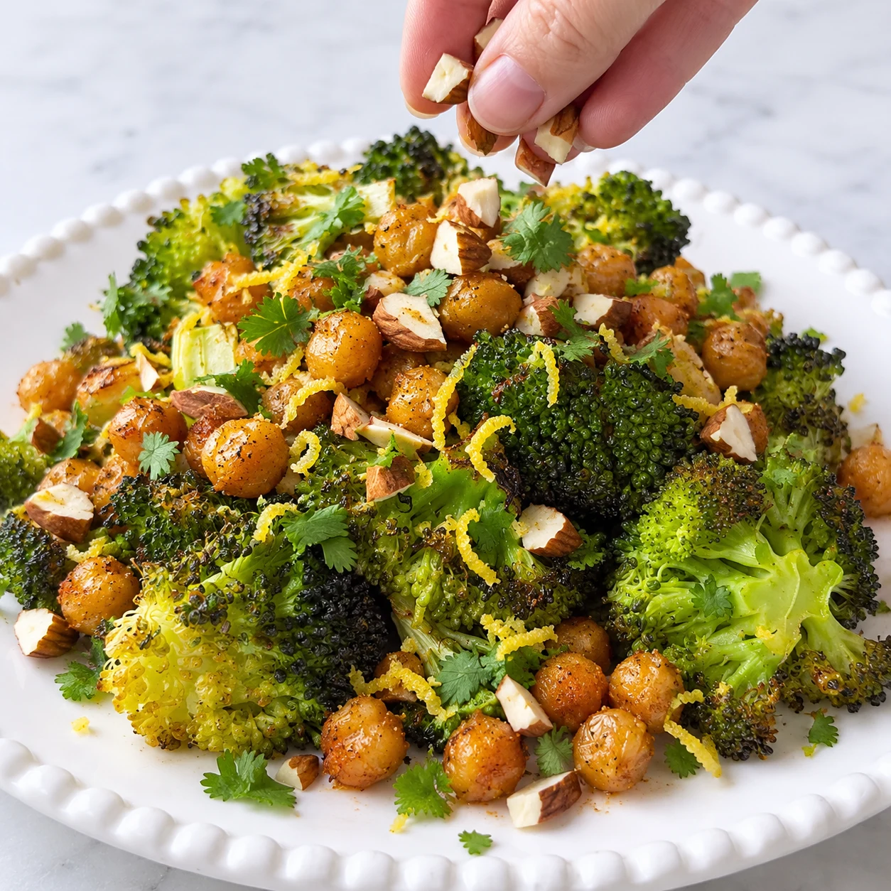Assiette brocoli pois chiches rôtis, main parsème petits morceaux amandes avec peau ; zestes fins et coriandre. Pas de sauce.