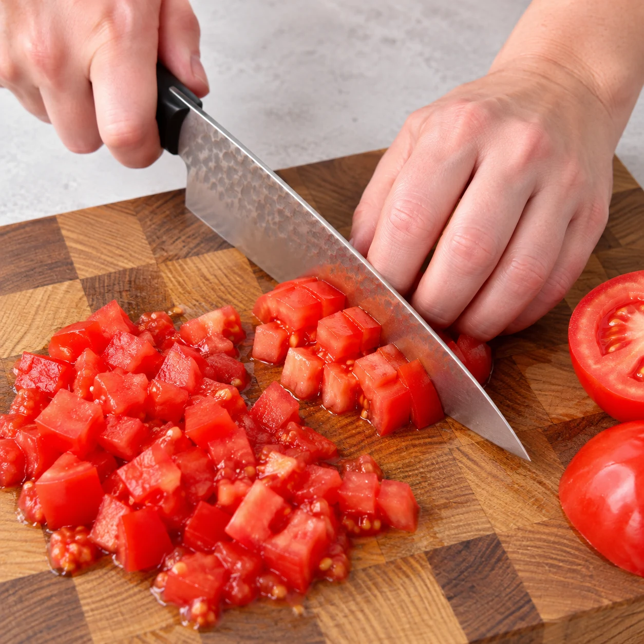 Découpe active d’une tomate rouge en petits dés, couteau et prise en griffe visibles.