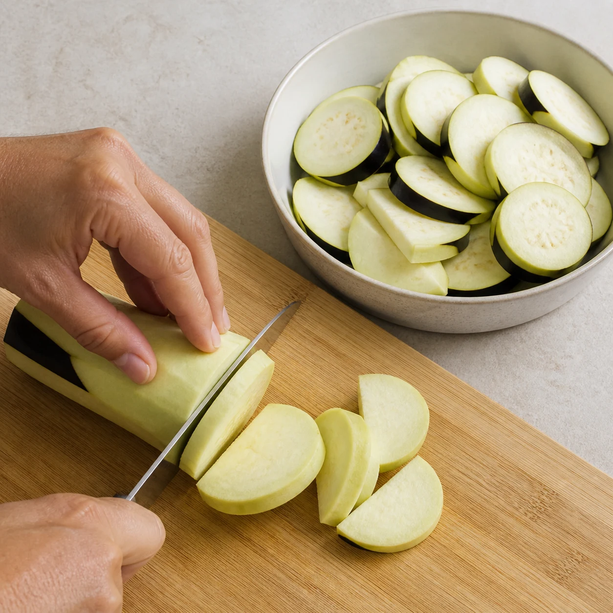 Rondelles et demi-rondelles d’aubergine crue régulières dans un plat séparé sur une planche claire.