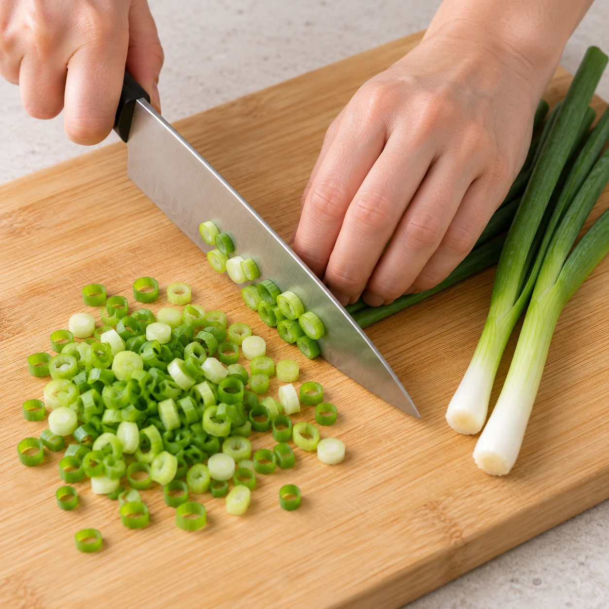 Émincez finement les trois branches de cébette et réservez-les pour la fin de cuisson. État attendu : Les cébettes sont découpées en petites rondelles. Une seule scène de cuisine, sans personne identifiable.