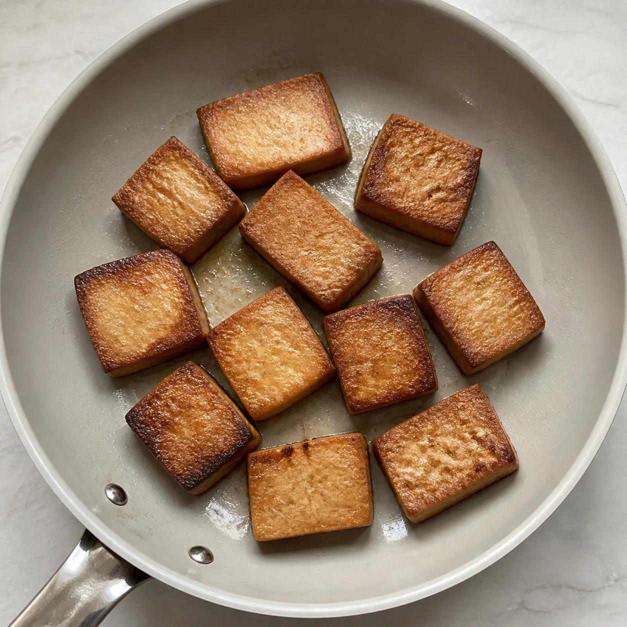Gros morceaux de tofu fumé dorés dans une poêle chaude.