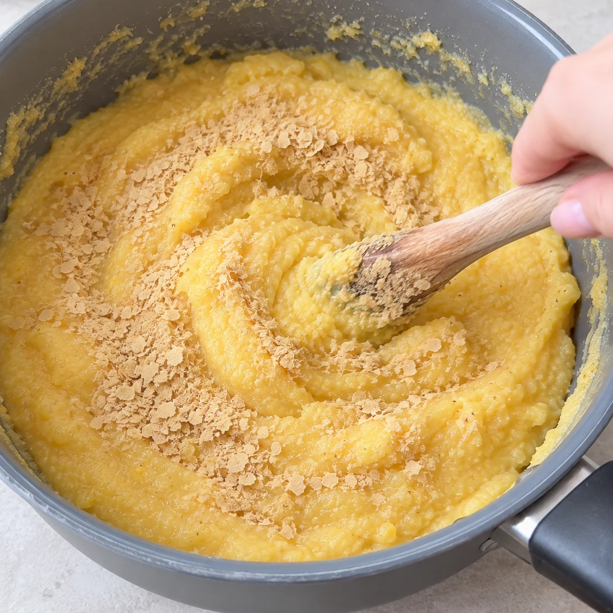 Paillettes beiges de levure maltée saupoudrées dans la polenta, spatule en bois ; aucun fromage.