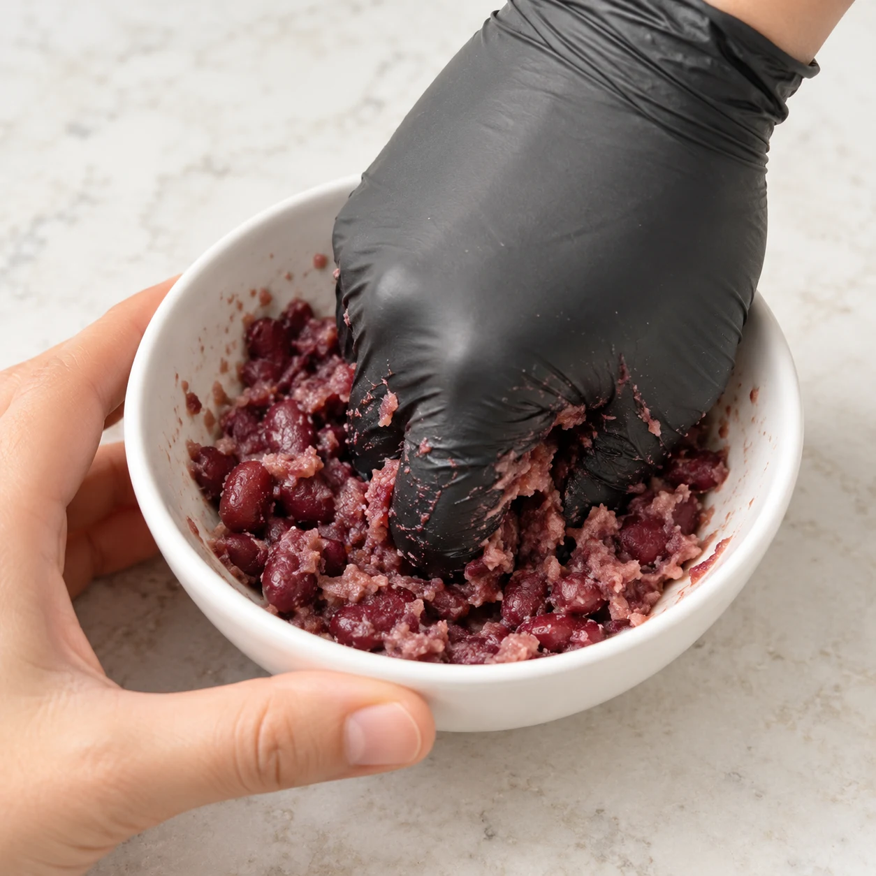 Main gantée écrasant quelques haricots rouges en conserve dans un petit bol.