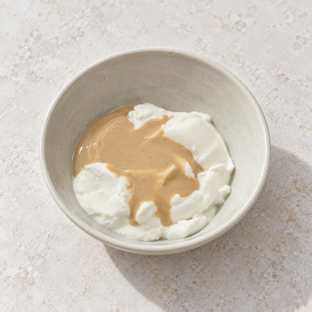 Tahini beige nappant le yaourt blanc ; deux ingrédients encore distincts.