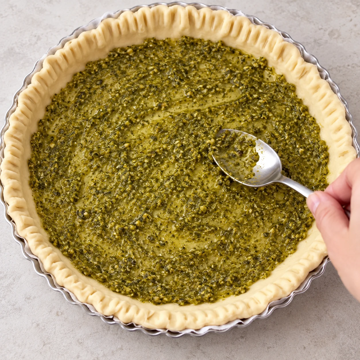 Étaler le pesto au miso : Une fine couche verte couvre régulièrement le fond de pâte. Ingrédients finaux uniquement, une seule action, photographie carrée réaliste.