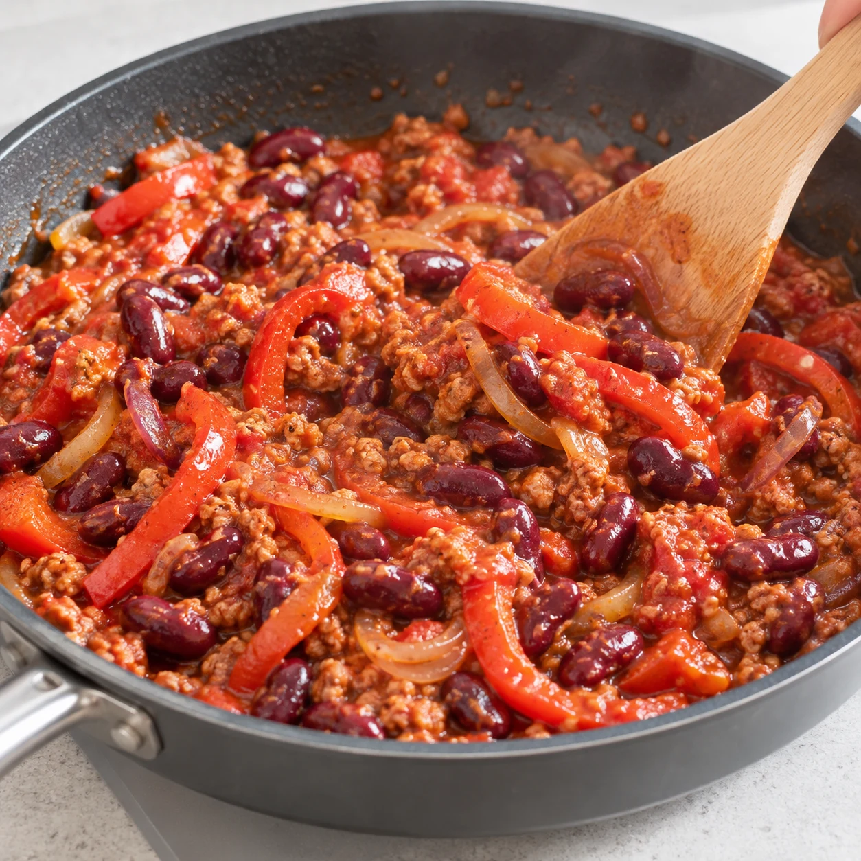 Spatule remuant doucement le mélange complet avec haricots entiers brillants, tomate réduite consistante et poivrons ; pas de persil encore.
