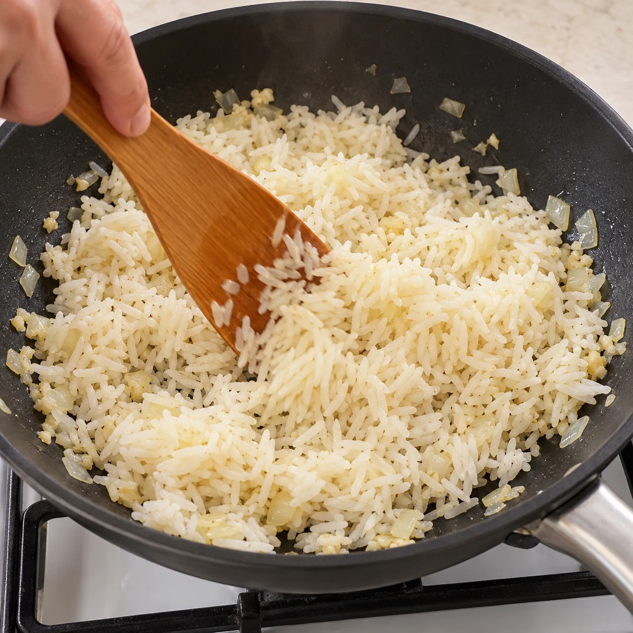 Incorporez les 400 g de riz déjà cuit et froid, idéalement de la veille. Remuez à la spatule en séparant les amas jusqu’à ce que les grains soient détachés et le riz bien chaud. Résultat visuel : Le riz est chaud et les grains sont séparés. Montrer seulement les ingrédients de cette étape, sur plan de travail pierre pâle ; pas de viande, pas d’œuf, pas de tofu.
