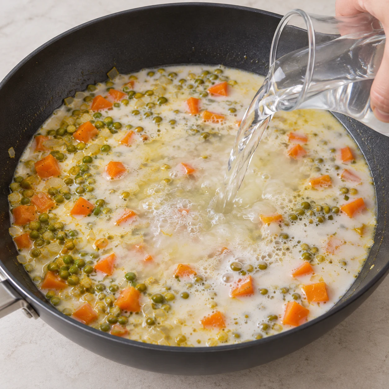 Eau claire versée avec une carafe neutre dans le lait de coco avec pois et carottes, pas encore de cube.