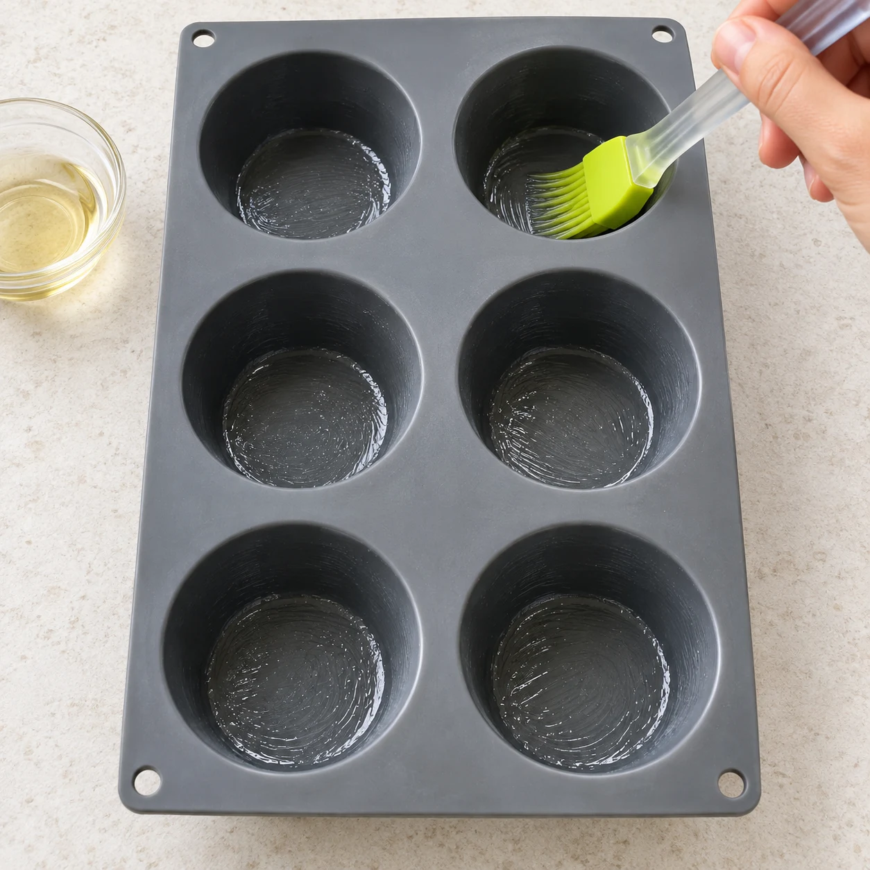 Un pinceau huile un moule gris en silicone à six gros muffins.