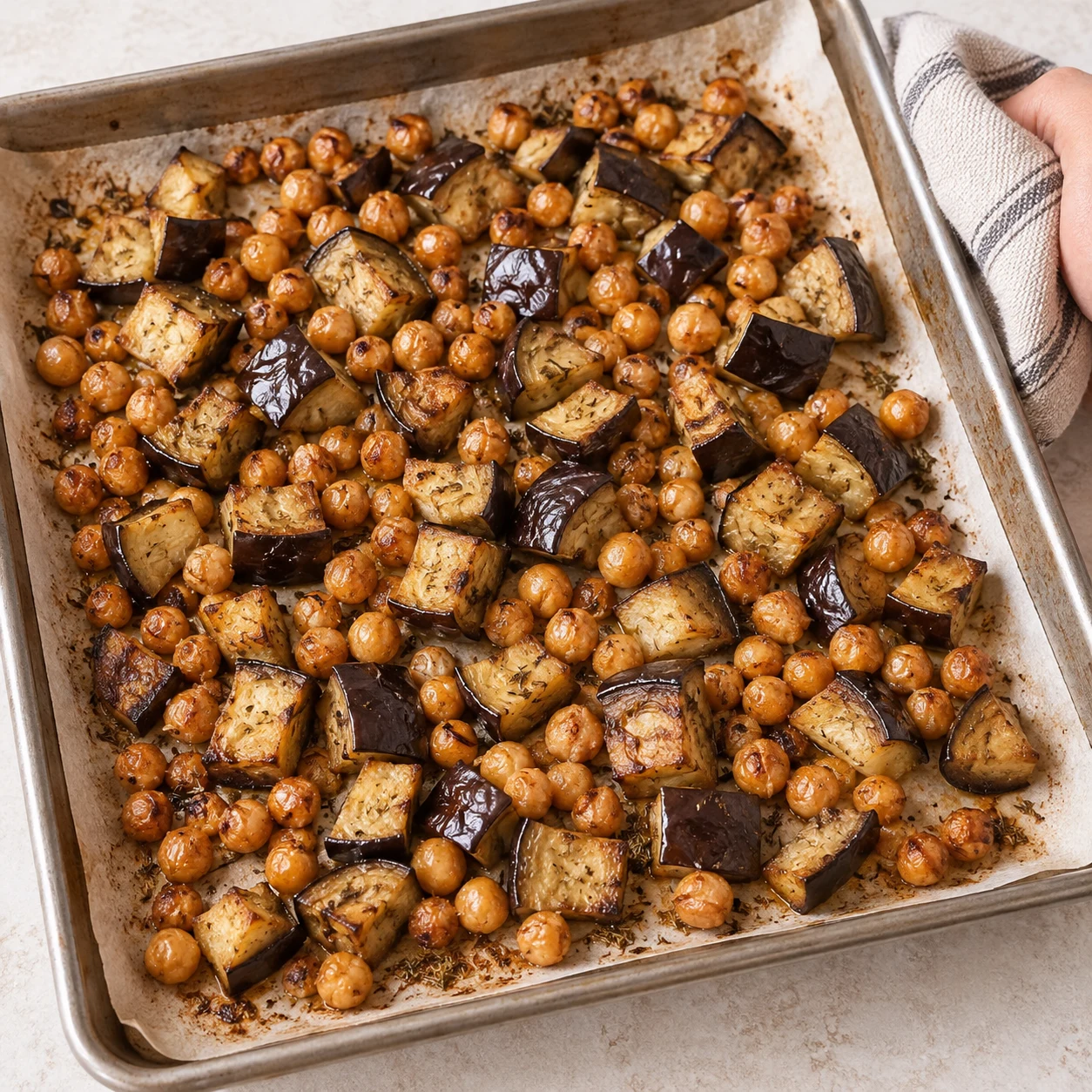 Plaque sortie du four avec cubes d’aubergine tendres et pois chiches grillés ; aucune tomate ni galette sur la plaque.