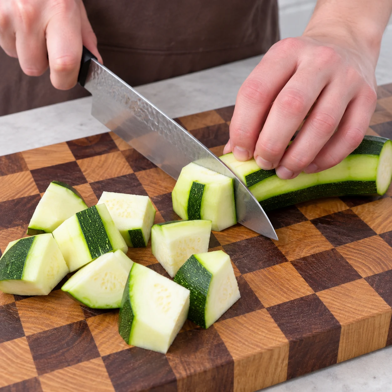Découpe active d’une courgette partiellement pelée en gros morceaux, bandes de peau verte conservées, prise sûre.