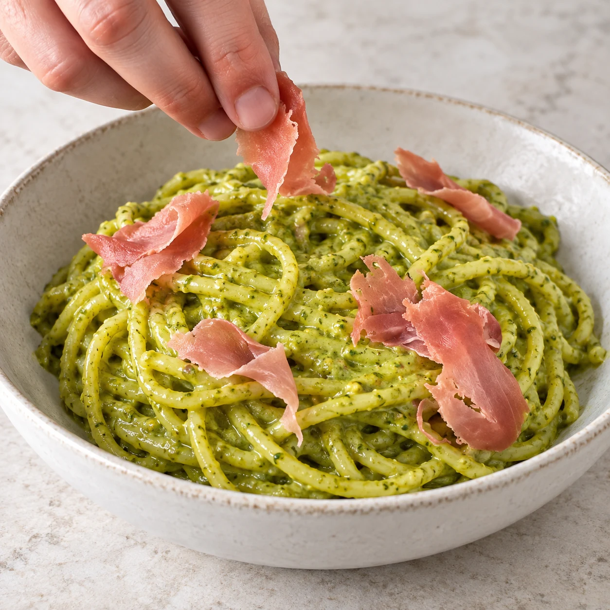 Mains adultes anonymes déposant quelques morceaux roses fins de jambon végétal sur les spaghetti verts, pas encore de crème blanche.