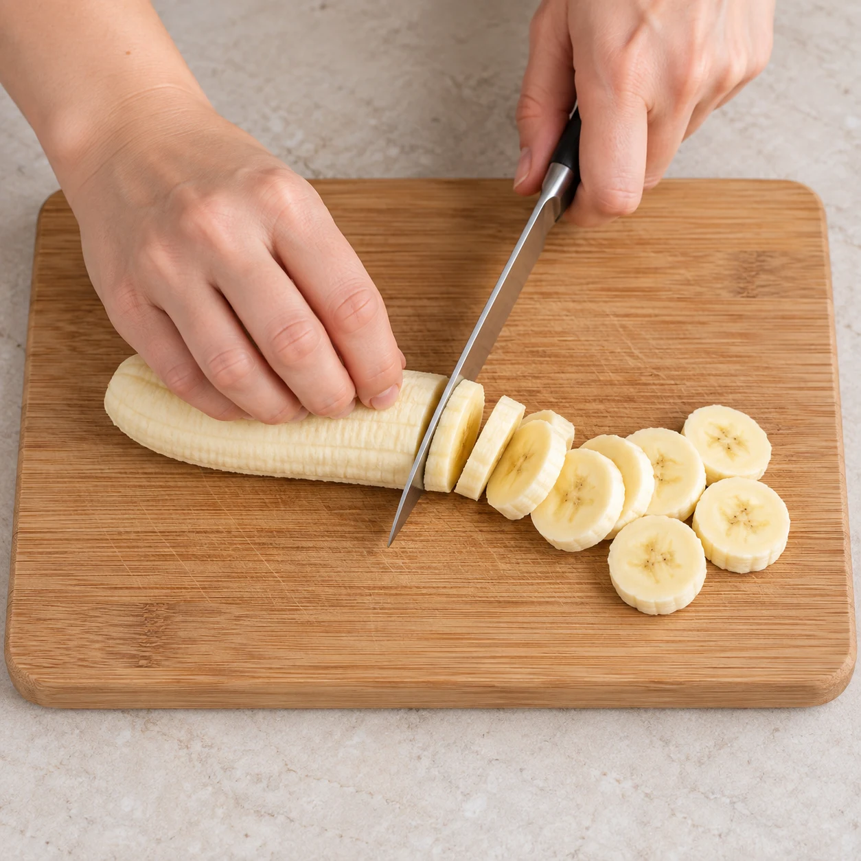 Main anonyme coupant une banane en rondelles avec une prise en griffe sûre.